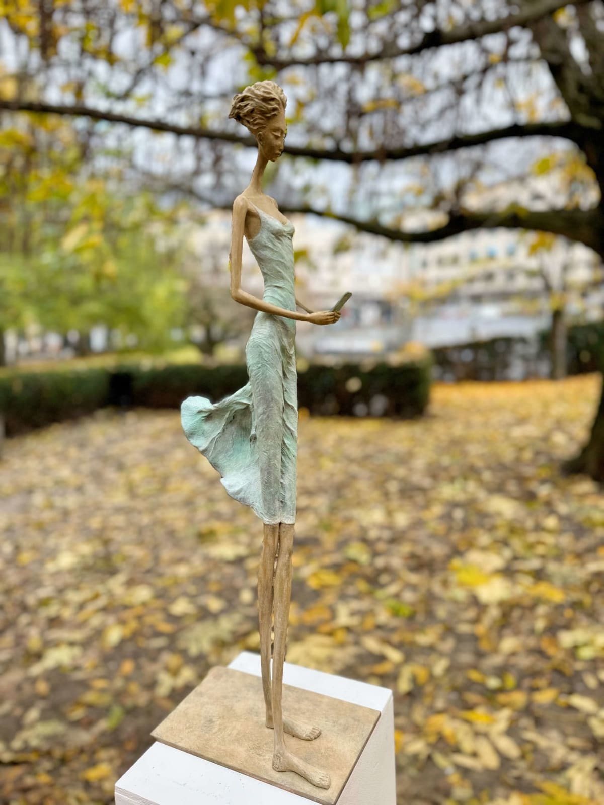 En attendant un signe sculpture d'Hedwige Leroux une sculpture de fille sculpture contemporaine sculpture de femme contemporaine sculpture en bronze une jeune fille marchant dans sa robe verte et tapotant sur le téléphone pour attendre un message Galerie Art Yi Galerie d'art de Bruxelles