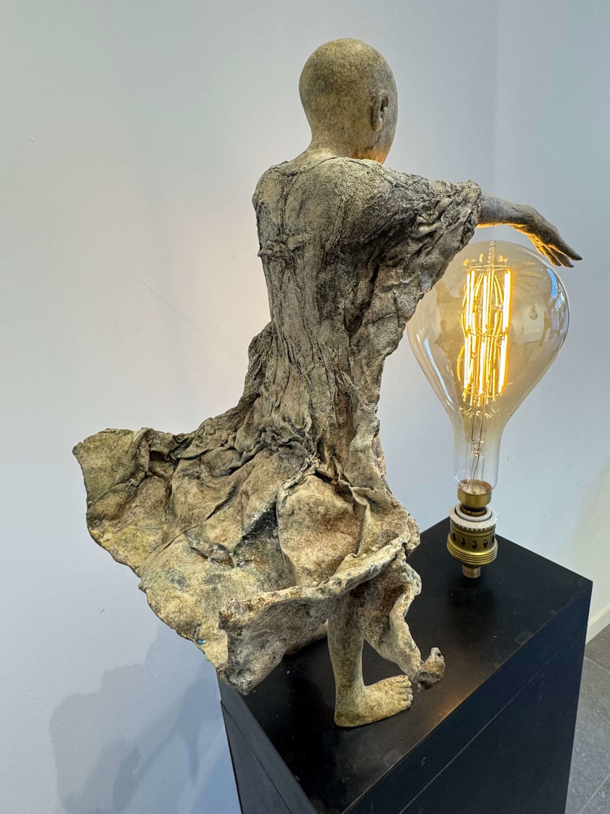 Visionary XL, sculpture lumineuse en bronze de Lieven d'Haese représentant un garçon ouvrant les bras pour allumer une ampoule, symbole d'imagination, de magie et de rêve. Sculpture d'art contemporain, design lumineux et design d'intérieur, exposée à la galerie Art Yi à Bruxelles.