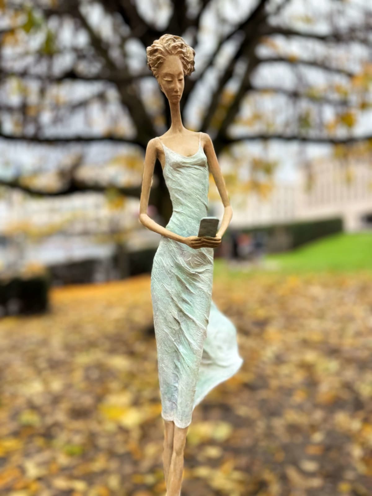 In attesa di un cartello scultura di Hedwige Leroux una ragazza scultura scultura contemporanea scultura donna contemporanea scultura in bronzo una giovane ragazza che cammina con il suo vestito verde e che chiama al telefono per aspettare un messaggio Galleria Art Yi Galleria d'arte di Bruxelles