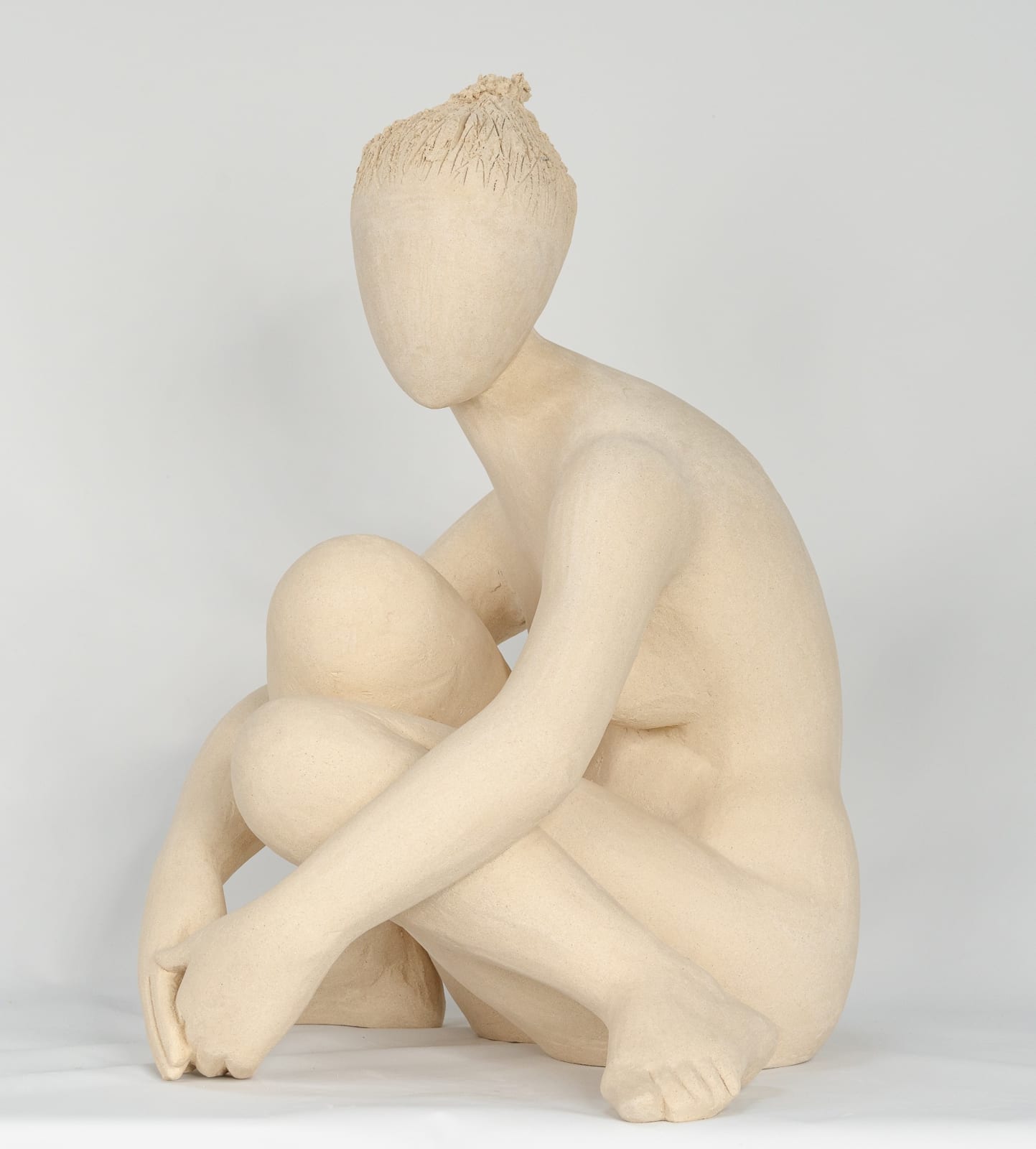 Seated white ceramic figure is looking over her left shoulder with arms draped around her knees which are tucked together.