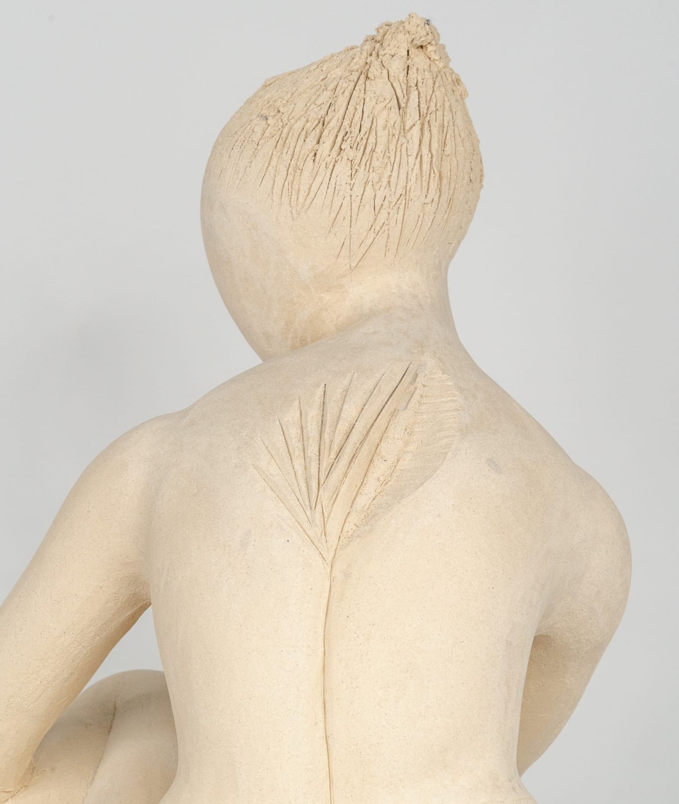 Seated white ceramic figure is looking over her left shoulder with arms draped around her knees which are tucked together.