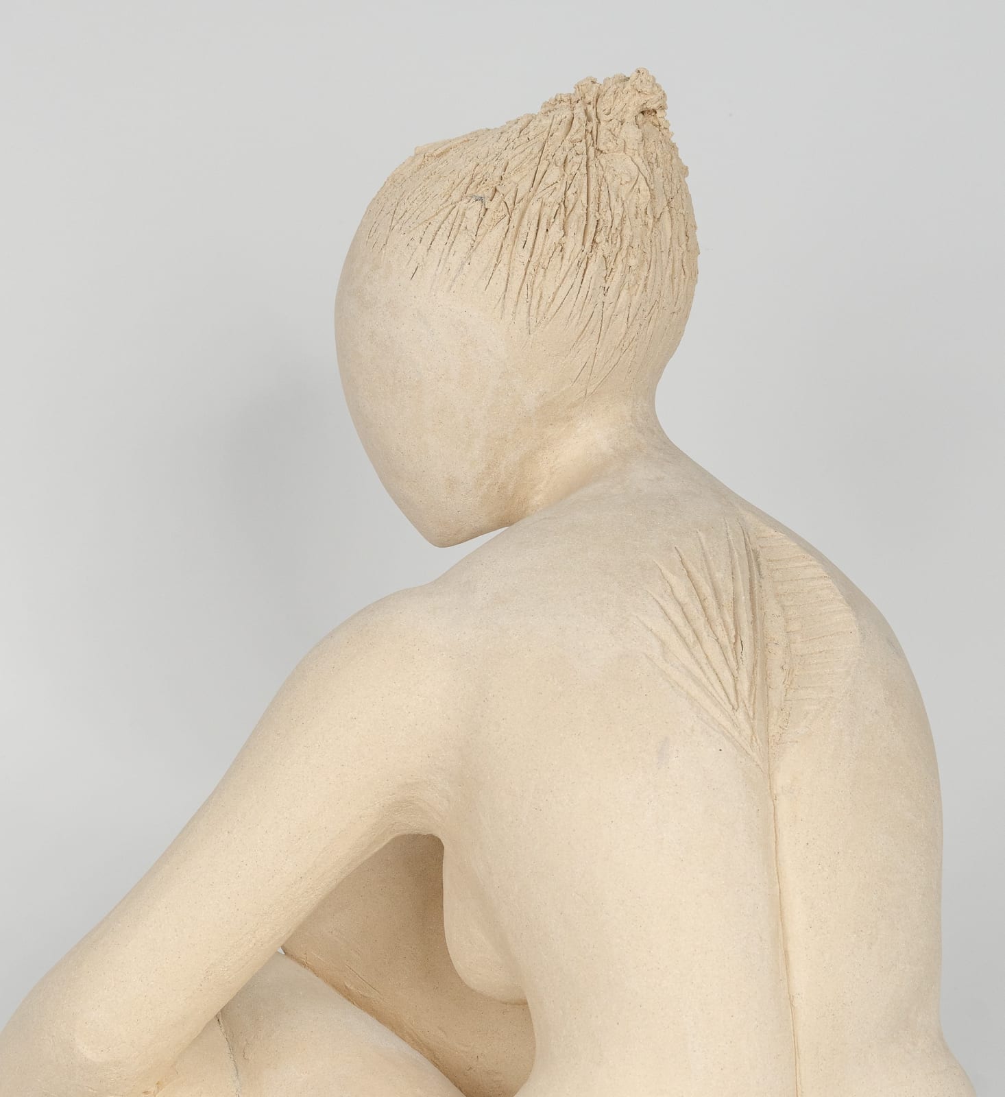 Seated white ceramic figure is looking over her left shoulder with arms draped around her knees which are tucked together.