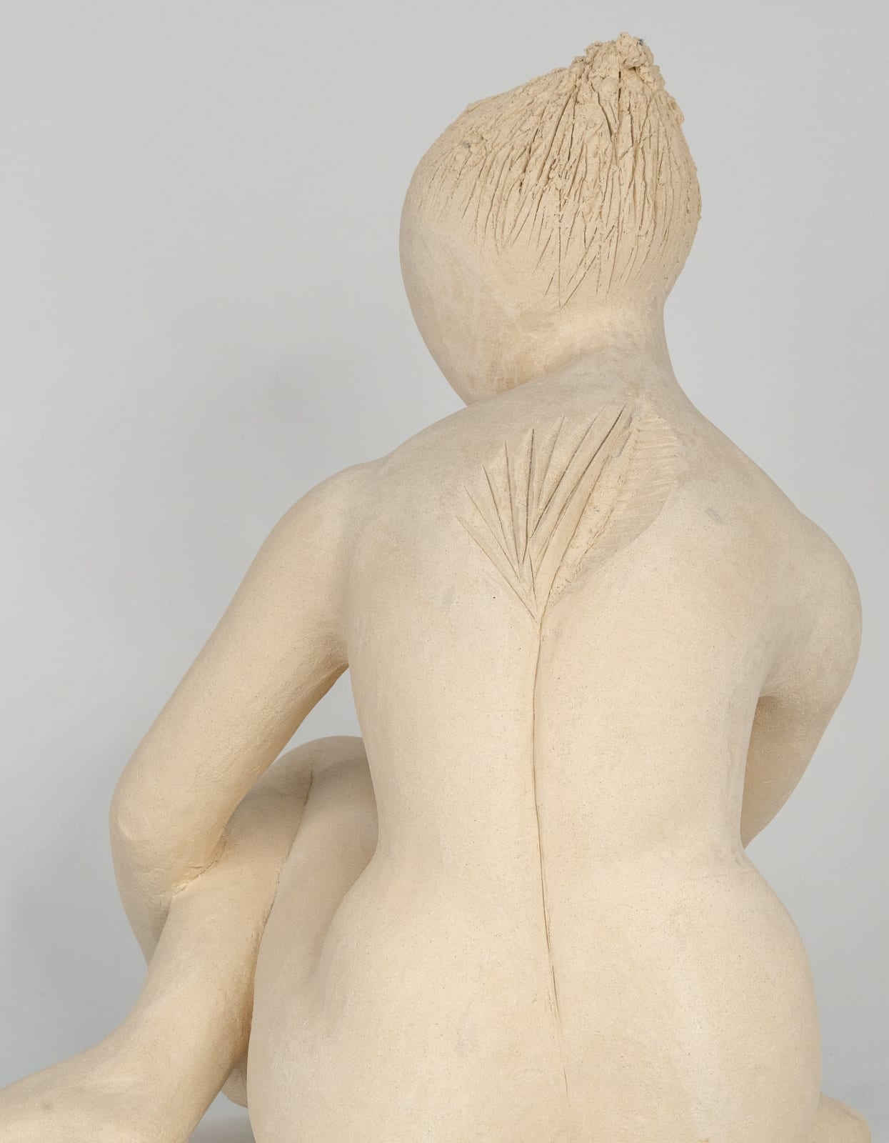 Seated white ceramic figure is looking over her left shoulder with arms draped around her knees which are tucked together.