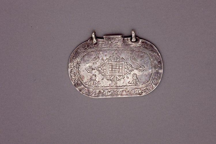 Silver oval talisman with central incised floral motif and Islamic inscription around the border