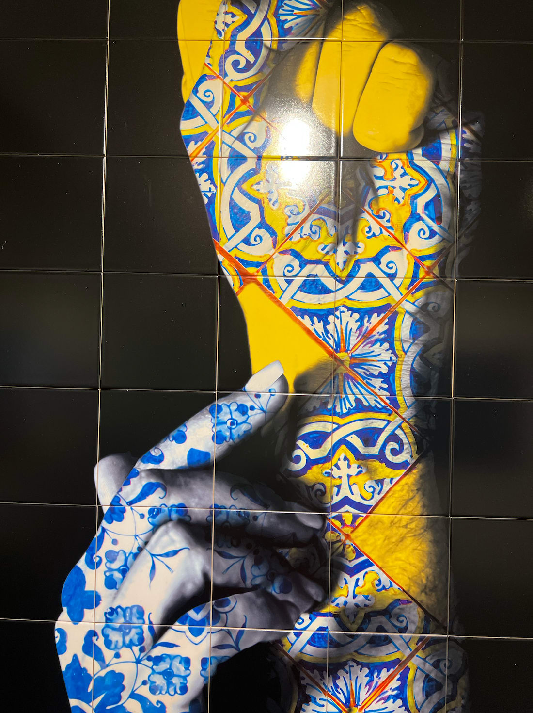 Detail photo of “Connexion”, limited edition print on Portuguese tile by O Gringo artist from Nice, France. Available at Carousel Fine Art Miami. The artist’s technique involves Fine Art prints on tiles, inspired by the tradition of 'Azulejos'—hand-painted tiles that adorn Mediterranean buildings. His mosaics reflect motifs from his expeditions, blending spiritual evocation, history, and modernity. Imbued with Portuguese culture and the melancholy of Fado, each piece tells a story through characters that evoke emotions from passion to deep melancholy. Colors of this work hues of: Blue, Red, Yellow, Green, Orange, White, Black