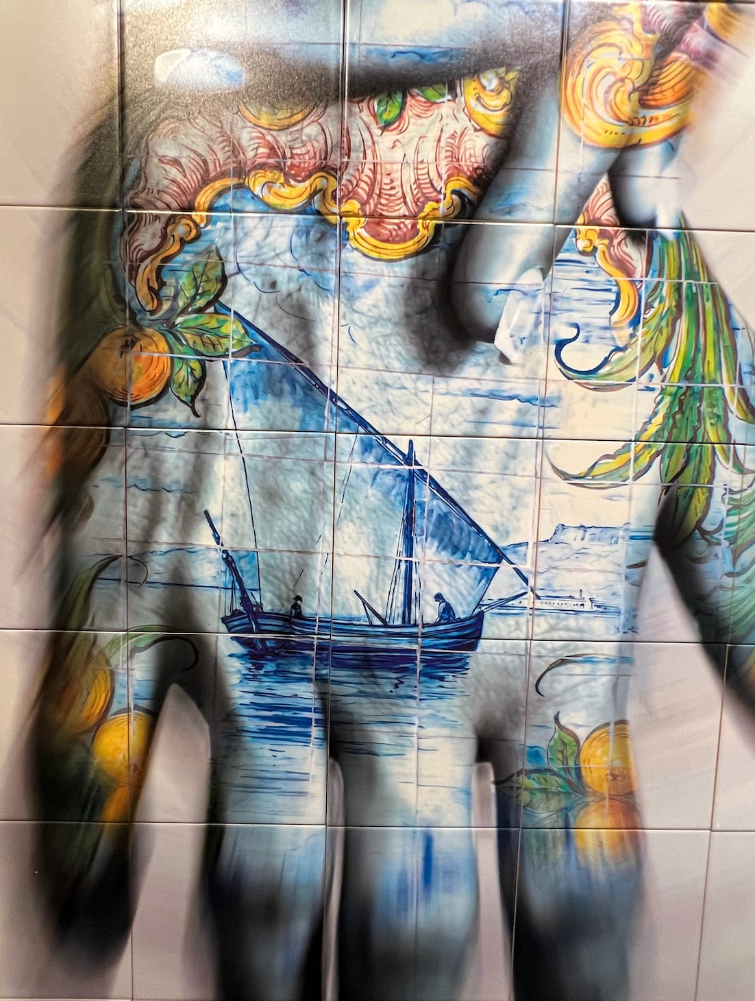 Detail photo of “Nos”, limited edition print on Portuguese tile by O Gringo artist from Nice, France. Available at Carousel Fine Art Miami. The artist’s technique involves Fine Art prints on tiles, inspired by the tradition of 'Azulejos'—hand-painted tiles that adorn Mediterranean buildings. His mosaics reflect motifs from his expeditions, blending spiritual evocation, history, and modernity. Imbued with Portuguese culture and the melancholy of Fado, each piece tells a story through characters that evoke emotions from passion to deep melancholy. Colors of this work hues of: Blue, Red, Yellow, Green, Orange, White, Black