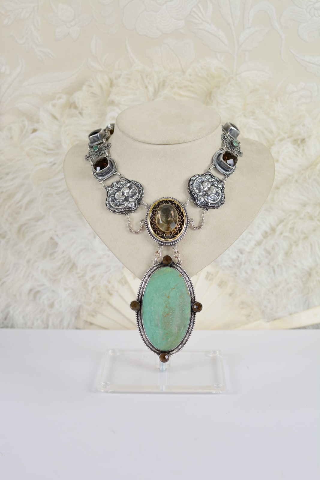 Jill Garber, A GRANDE CERRILOS TURQUOISE OVAL CUT CABOCHON IS MOUNTED WITHIN AN ELABORATE DOUBLE FRAME CONTAINING FOUR 68 MM ROSE CUT SMOKEY TOPAZ GEMSTONES