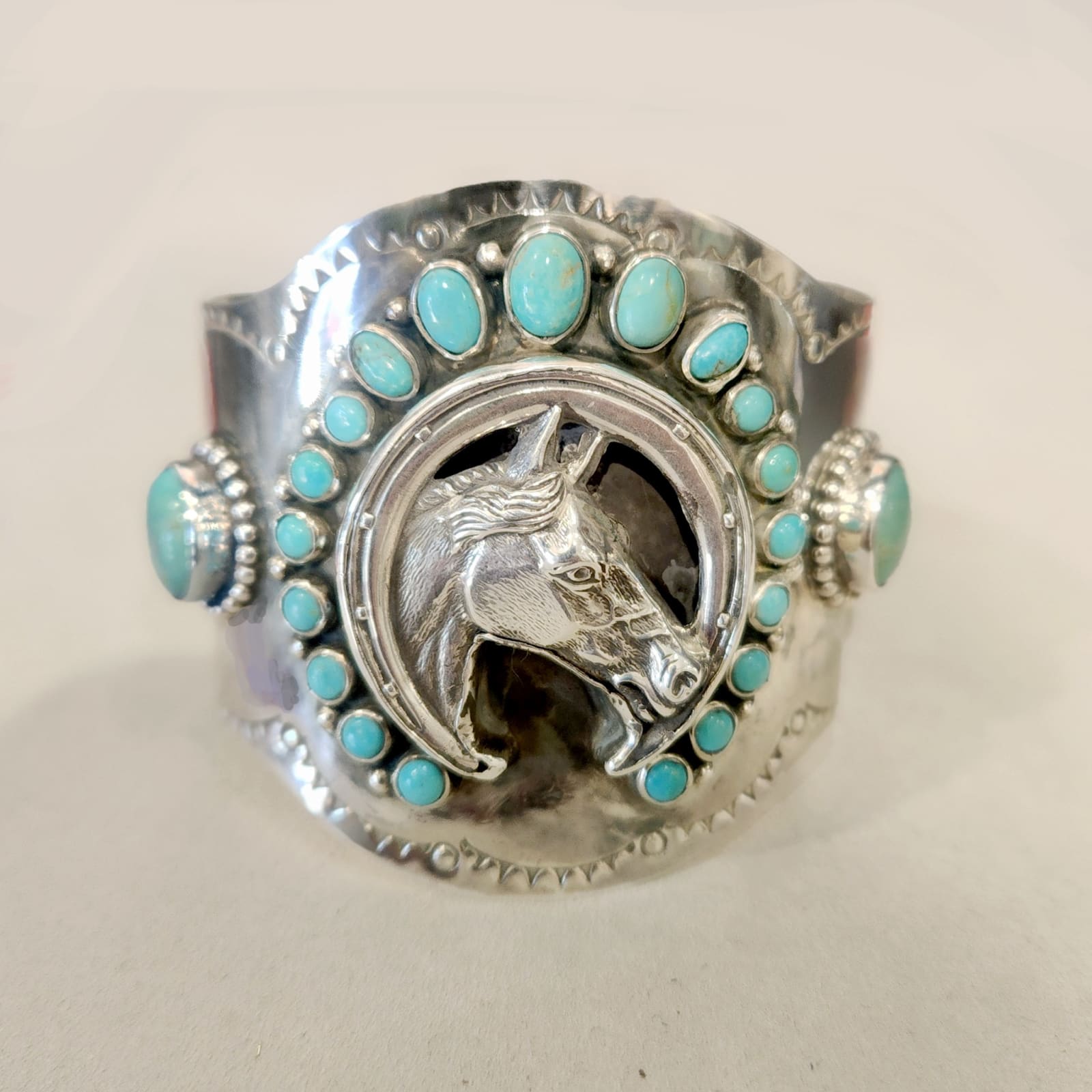 Jill Garber, A Western inspired Luck Boy cuff bracelet honoring Jill’s Doc Bar quarter Horse “Cash” is surrounded with a shoe shaped wreath of greenish aqua kingman turquoise cabochons