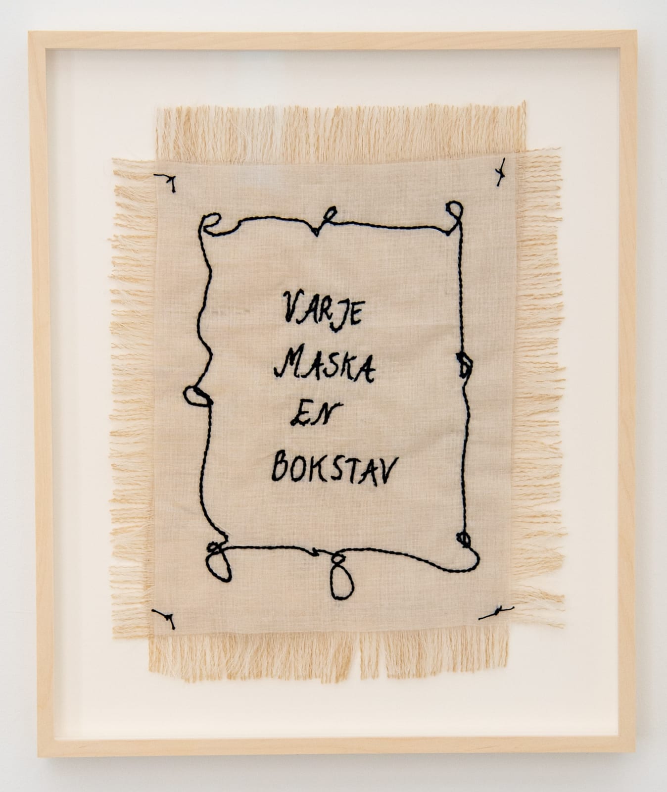 vitt tyg med broderade svarta bokstäver, varje maska en bokstav