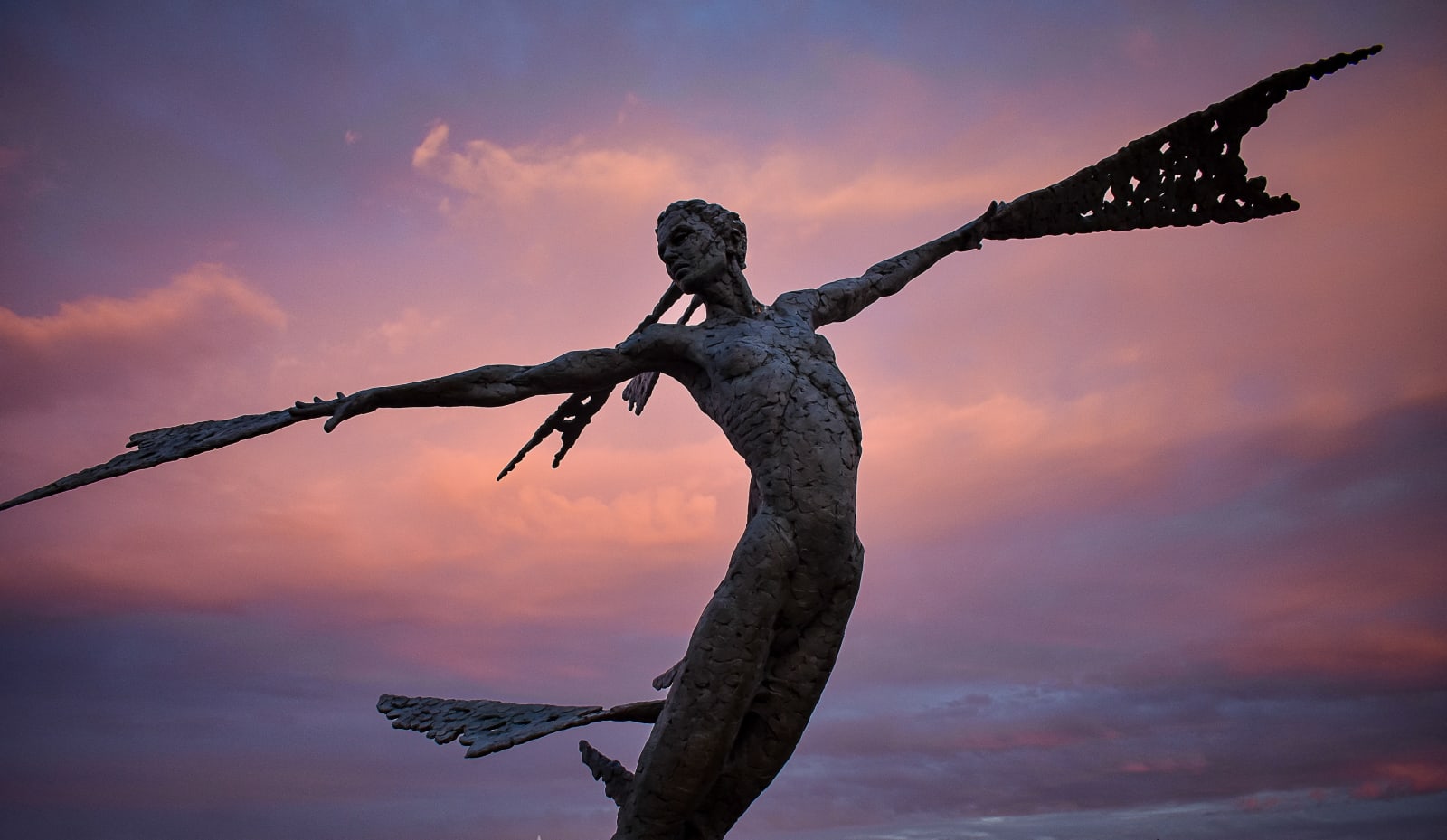 A monumental bronze sculpture of a winged female by Nicola Godden stands in front of a sunset at a Dorset sculpture park, Sculpture by the Lakes