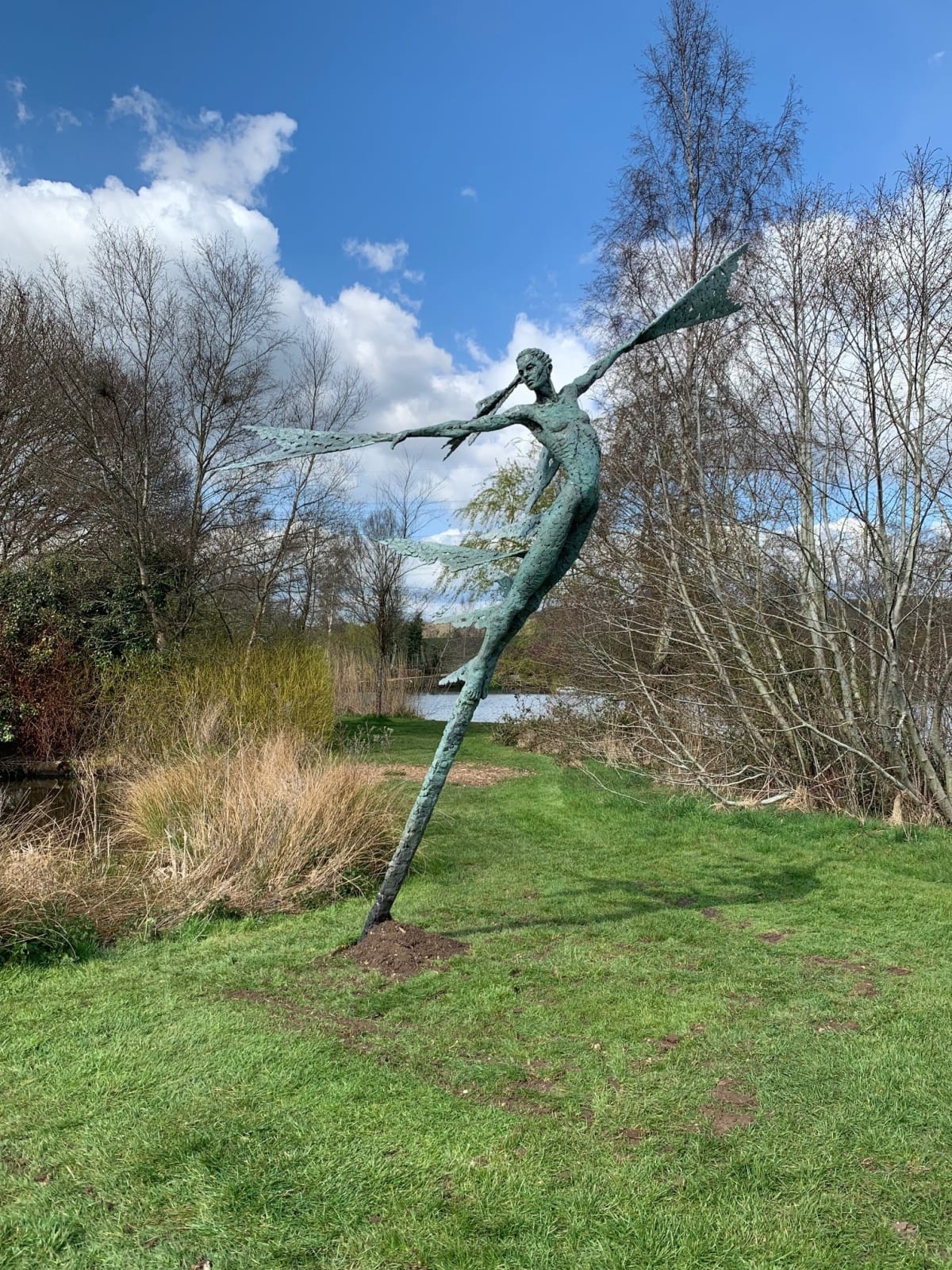 A monumental bronze sculpture of a winged female stands in front of trees at a Dorset sculpture park, Sculpture by the Lakes