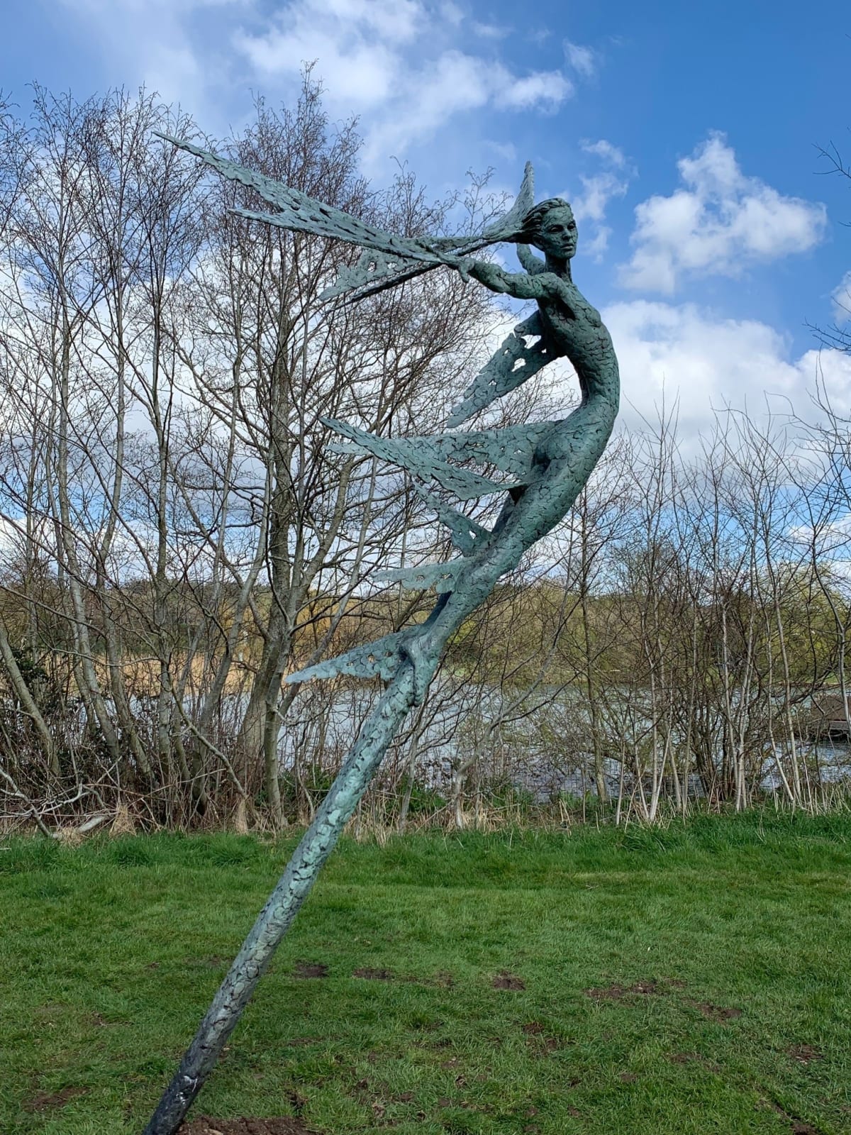A monumental bronze sculpture of a winged female stands in front of trees at a Dorset sculpture park, Sculpture by the Lakes