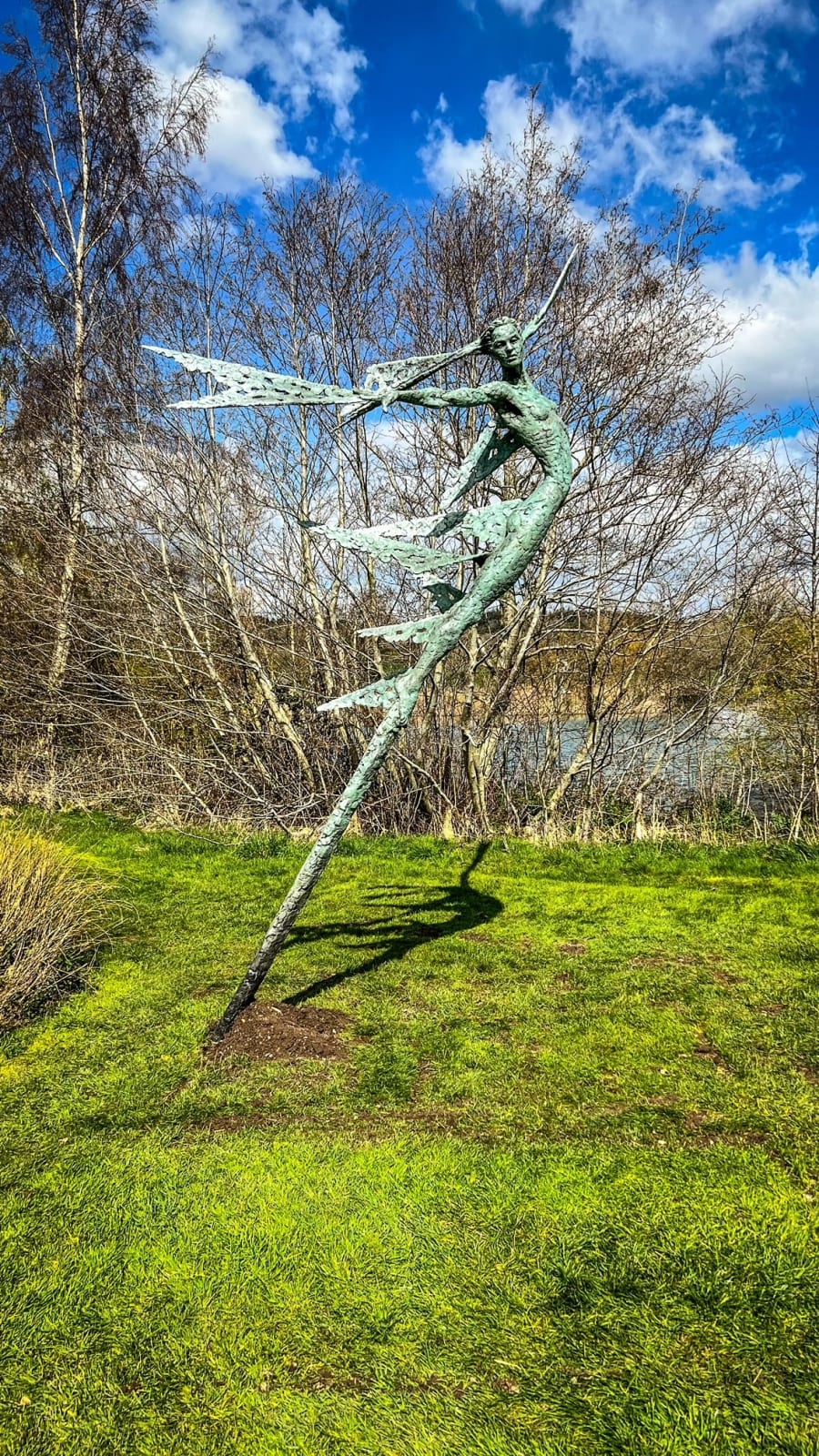 A monumental bronze sculpture of a winged female stands in front of trees at a Dorset sculpture park, Sculpture by the Lakes