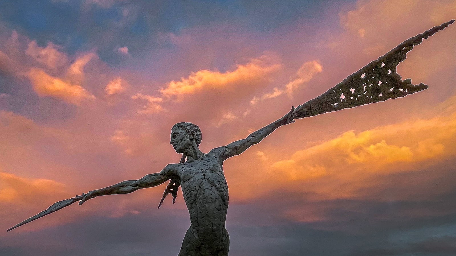 A monumental bronze sculpture of a winged female by Nicola Godden stands in front of a sunset at a Dorset sculpture park, Sculpture by the Lakes
