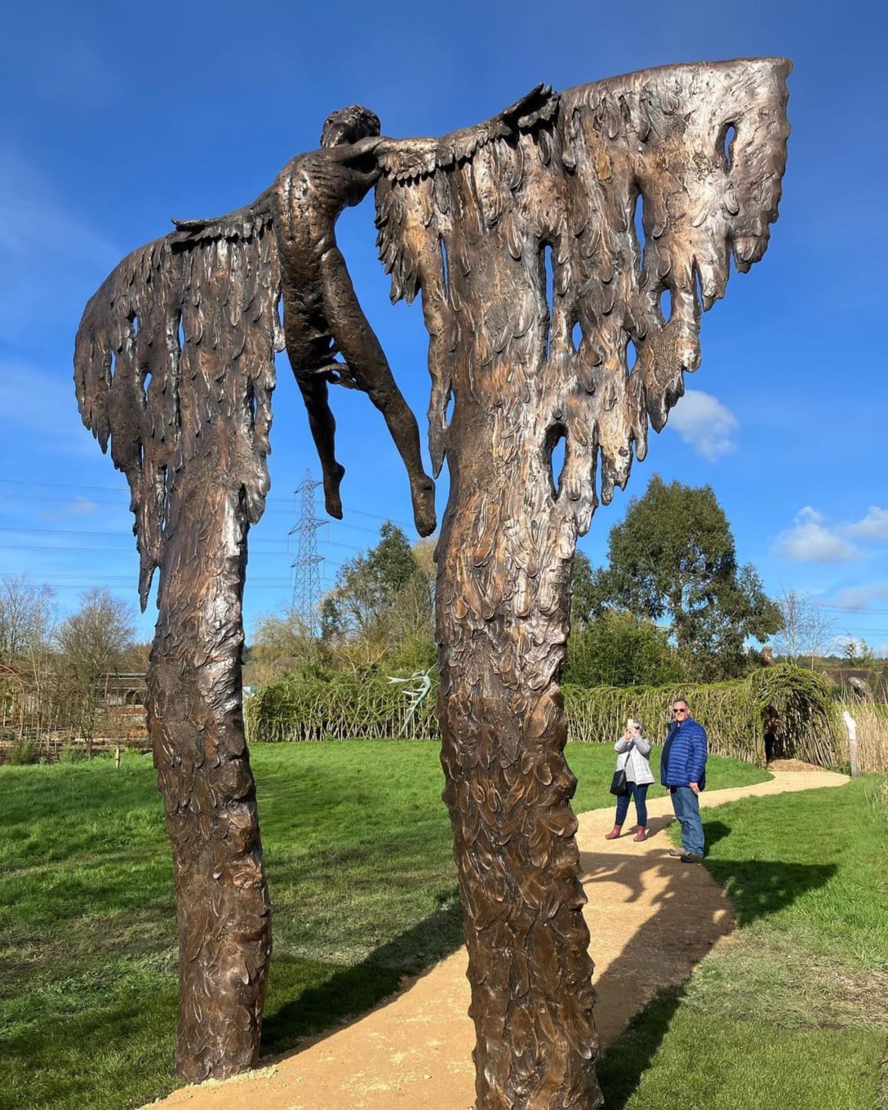 Two people are looking up at a monumental bronze sculpture of a mythological figure at a Dorset sculpture park.