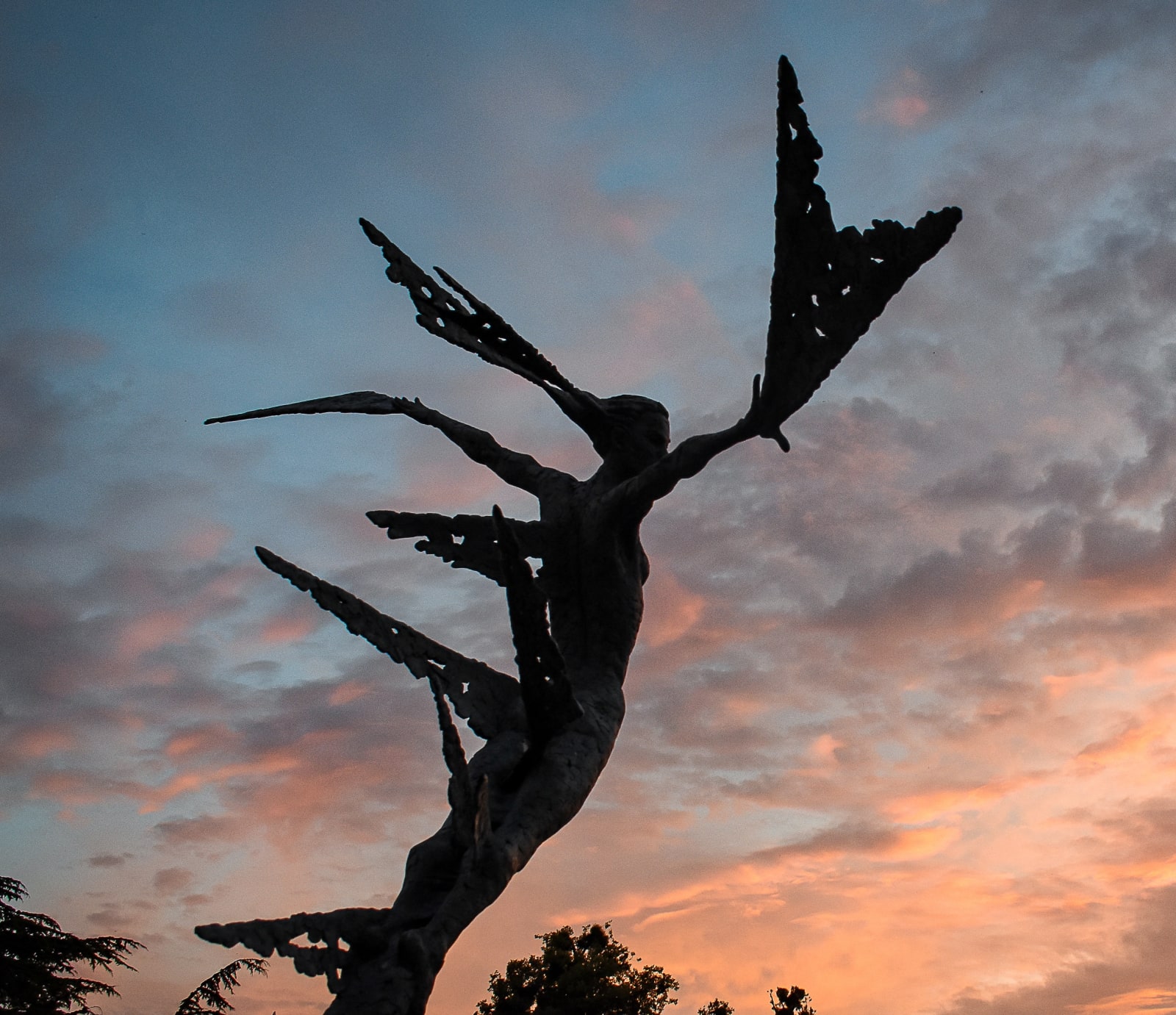 A monumental bronze sculpture of a winged female by Nicola Godden stands in front of a sunset at a Dorset sculpture park, Sculpture by the Lakes