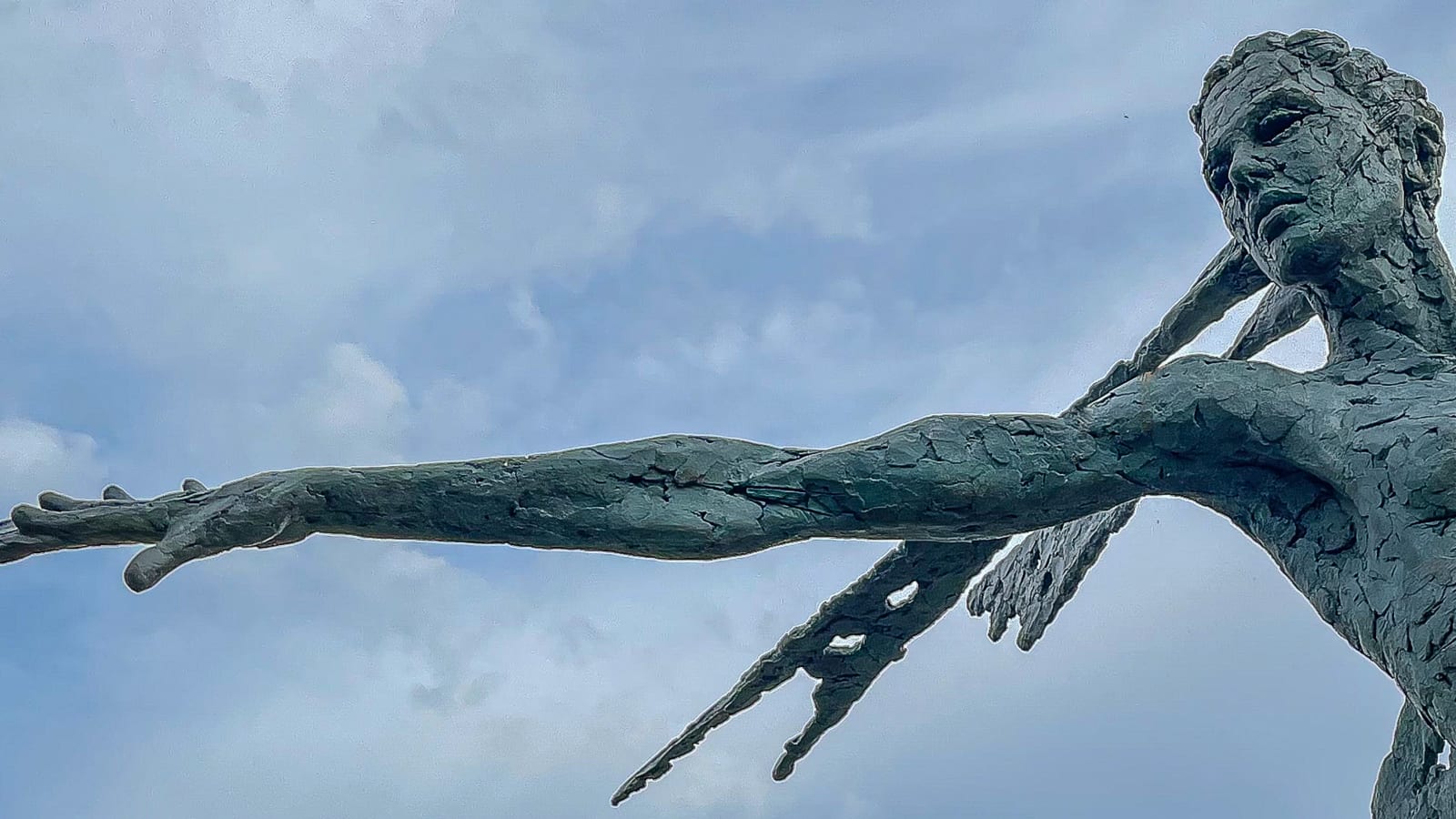A monumental bronze sculpture of a winged female stands in front of a willow walk at a Dorset sculpture park, Sculpture by the Lakes, close up