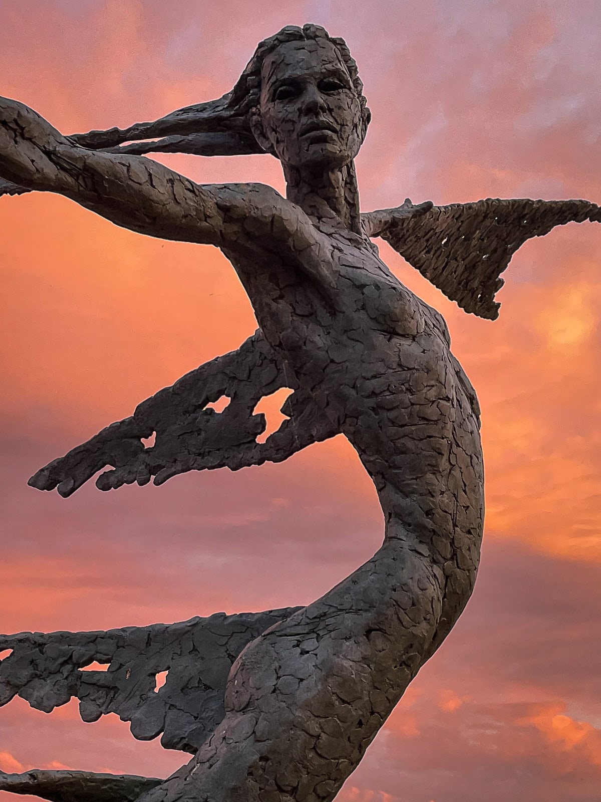 A monumental bronze sculpture of a winged female by Nicola Godden stands in front of a sunset at a Dorset sculpture park, Sculpture by the Lakes, close up of figure