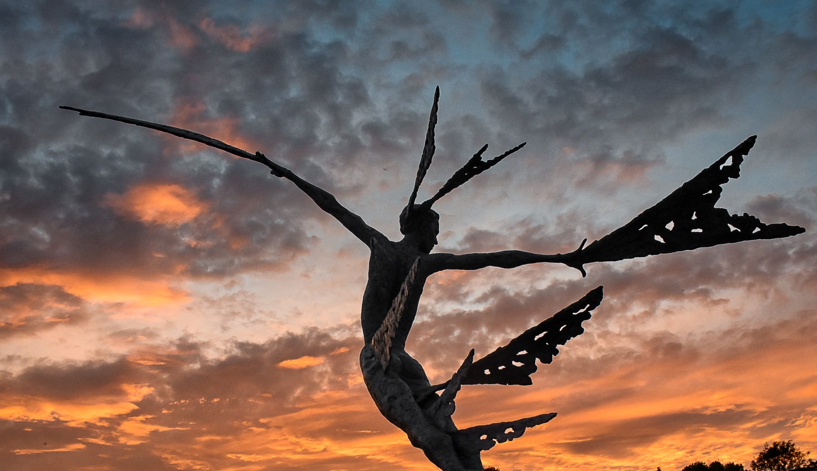 #A monumental bronze sculpture of a winged female by Nicola Godden stands in front of a sunset at a Dorset sculpture park, Sculpture by the Lakes