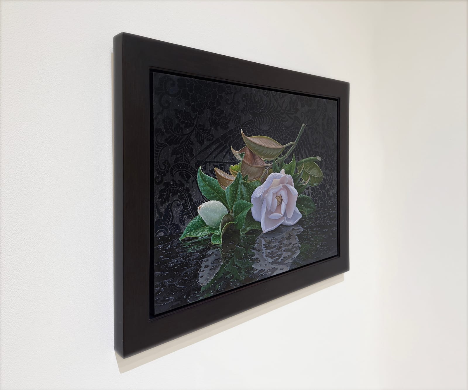 hyper-realistic painting of a single magnolia blossom that has fallen onto a reflective ground. Water droplets and small puddles reflect the flower.