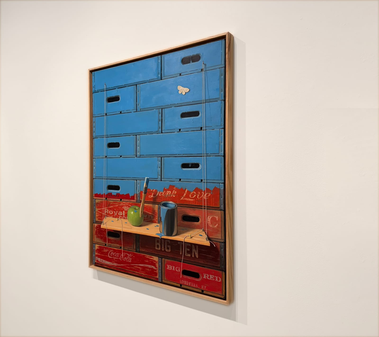 Painting of stacked crates and an apple with a bucket of paint