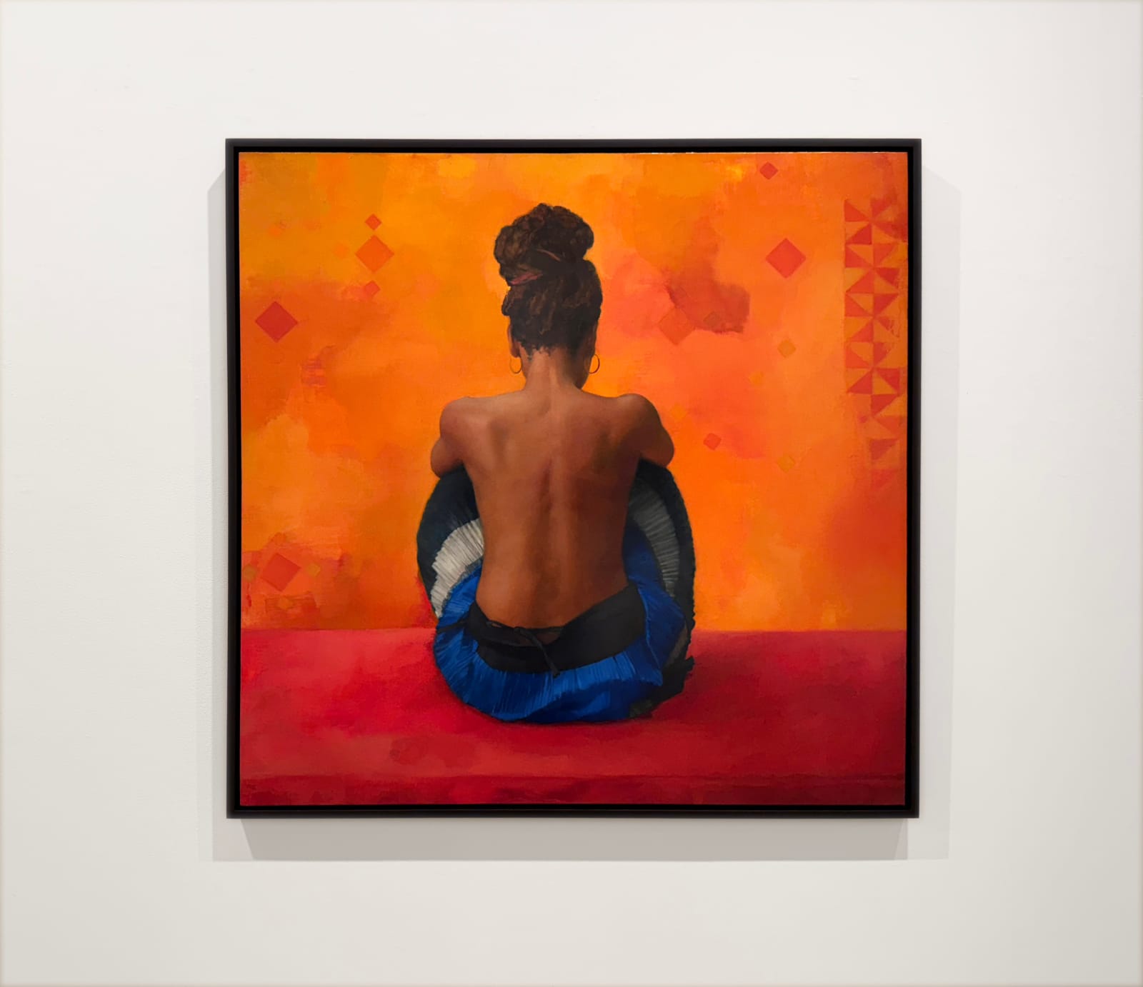 Painting of a woman with brown skin and hair in a bun sitting in a blue skirt with orange background