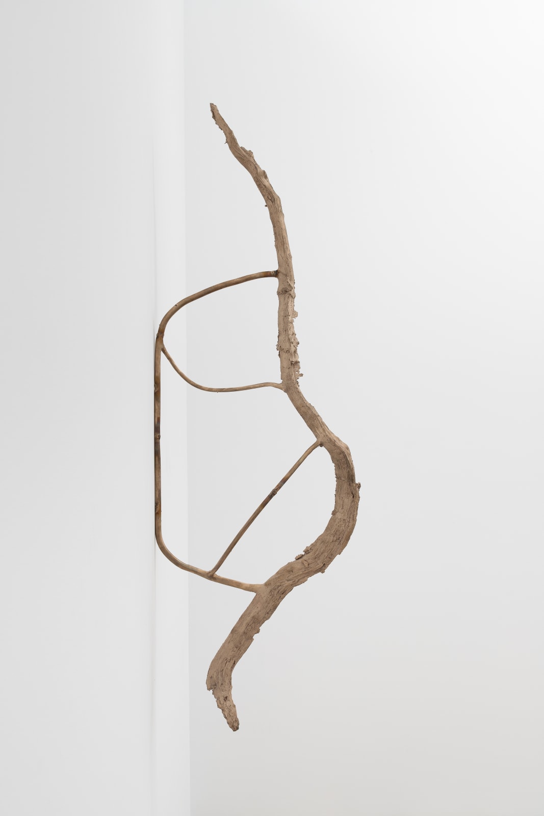 installation view of a spindly bronze sculpture mounted to the wall