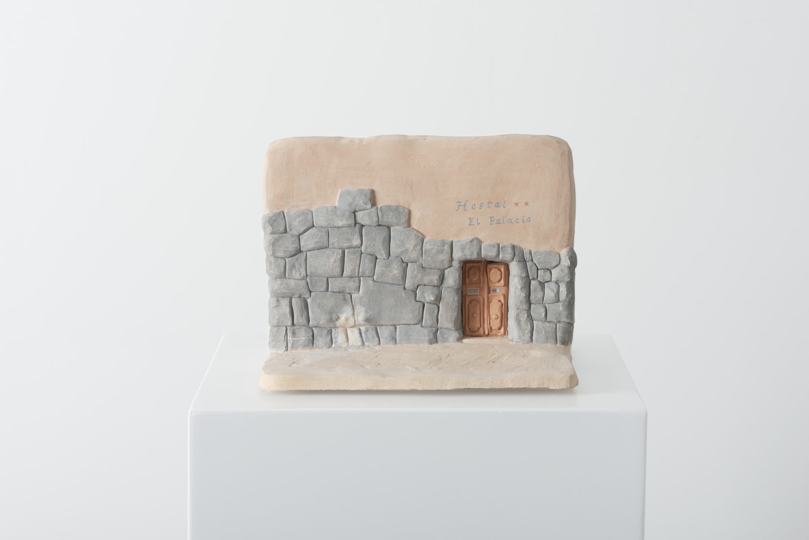 small ceramic piece modeling a wall and floor -- on one side of the wall is a door through the Peruvian twelve-angled-stone wall, above which is text reading 