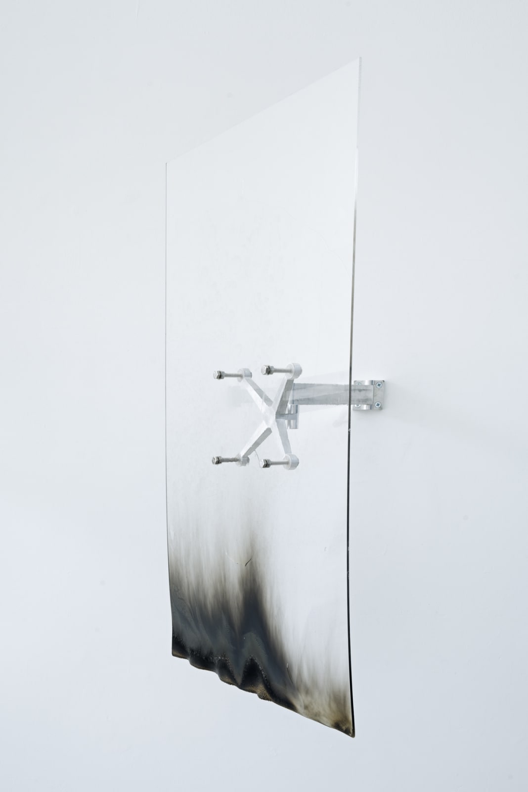 An image of a burned acrylic sheet attached to an aluminum spider arm against a white wall.