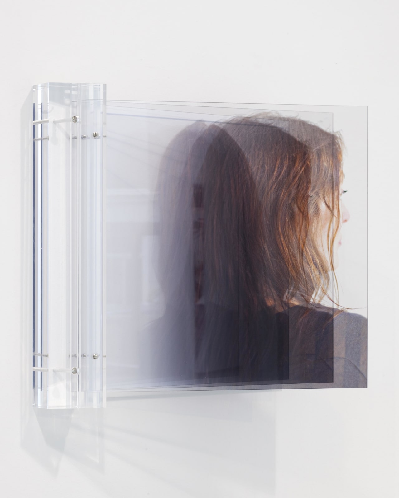 An ethereal print of a woman facing the opposite direction in between two sheets of plexiglass.