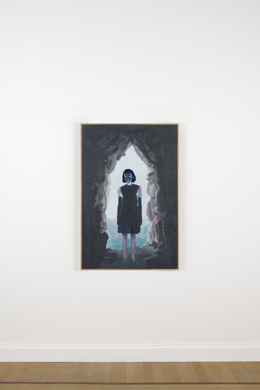 exhibition image of an oil painting depicting a color negative figure standing in the entrance of a cavern, lit from behind