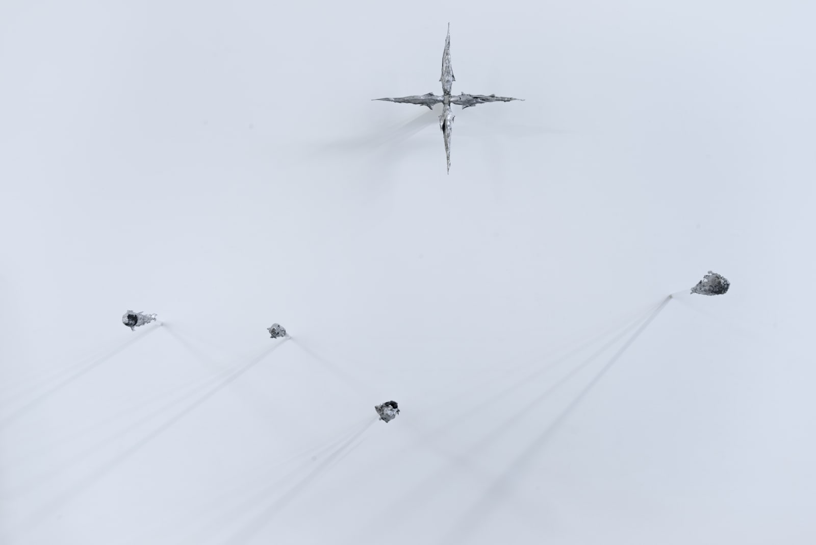 An image of aluminum fish fossils and fragments shaped into a star hanging from a white wall.