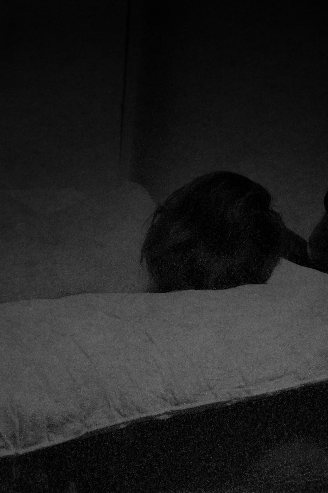 A black and white inkjet print depicting a figure sleeping in a bed.