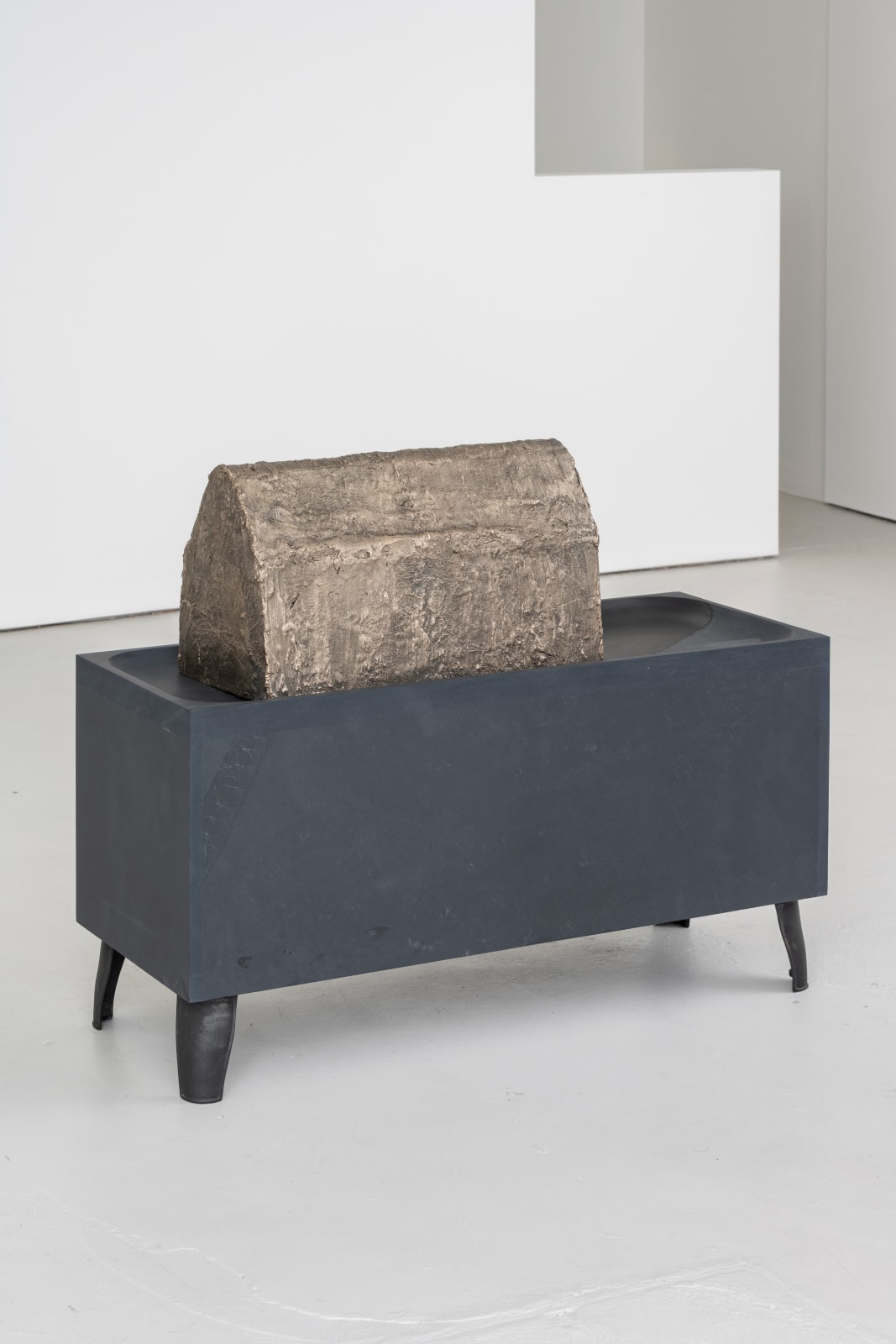 a cast iron box that has four small legs elevating it like a table, with a rounded bronze figure that comes to a point sitting on top of it.