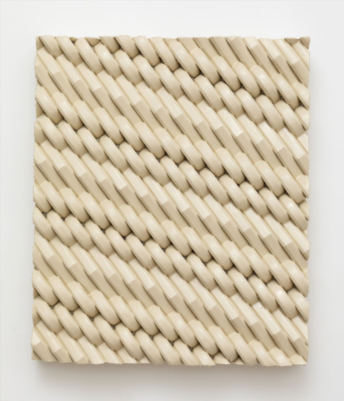Wall-mounted sculpture consisting of carved polystyrene pieces aggregated together to form a cream hued, interlocking patterned rectangular panel. 