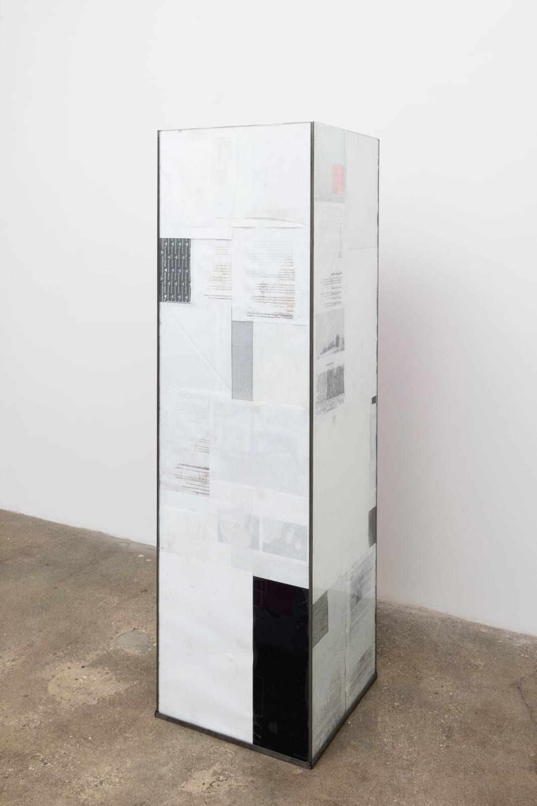 Free-standing sculpture of a long square column of glass with notes and document papers adhered on the inside, rendering it opaque. 