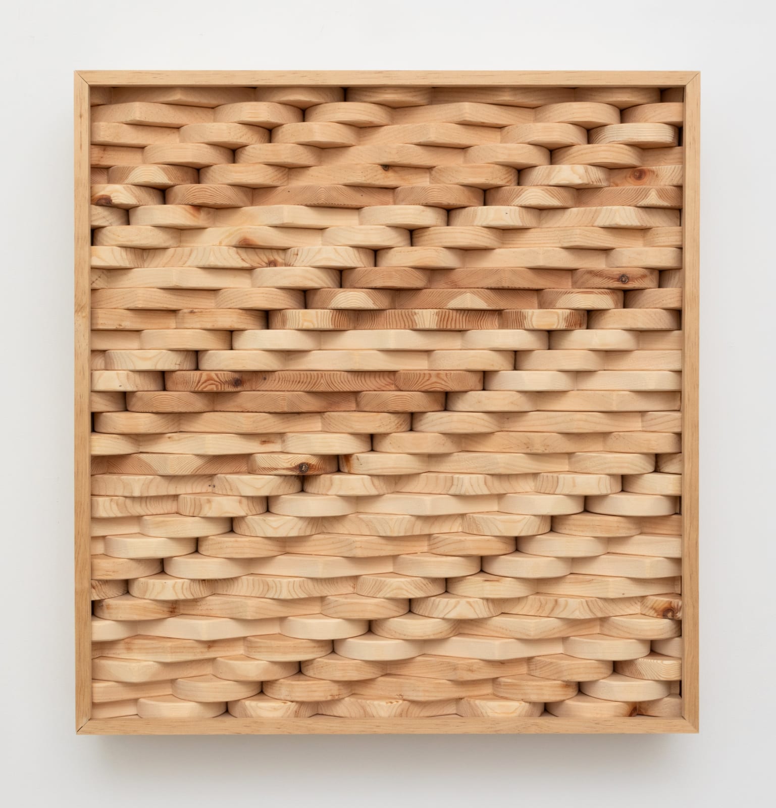 Wall-mounted sculpture consisting of carved wooden pieces aggregated together to form an interlocking patterned rectangular panel.