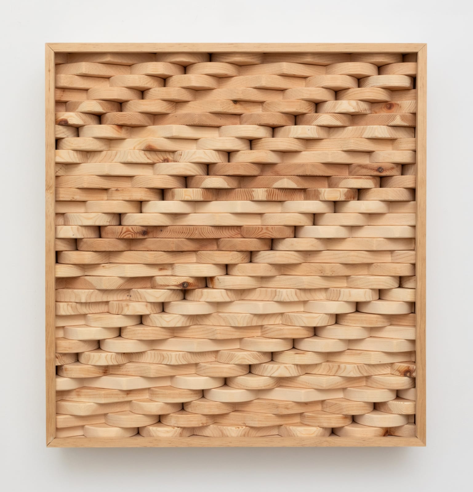 Wall-mounted sculpture consisting of carved wooden pieces aggregated together to form an interlocking patterned rectangular panel.