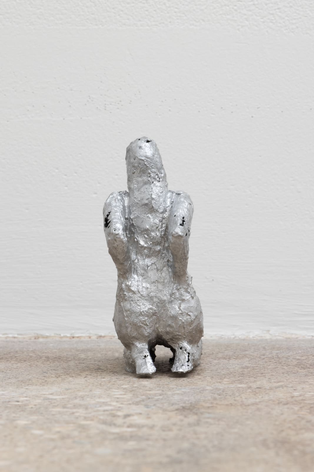 Free-standing sculpture made from lost-wax cast aluminum featuring a kneeling human figure with hands on hips and elbows jutting back.