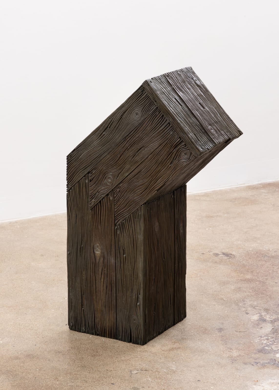 Free-standing bronze sculpture in the form of a wooden beam bent at a 45-degree angle toward the top, cast with a surface texture resembling wood grain
