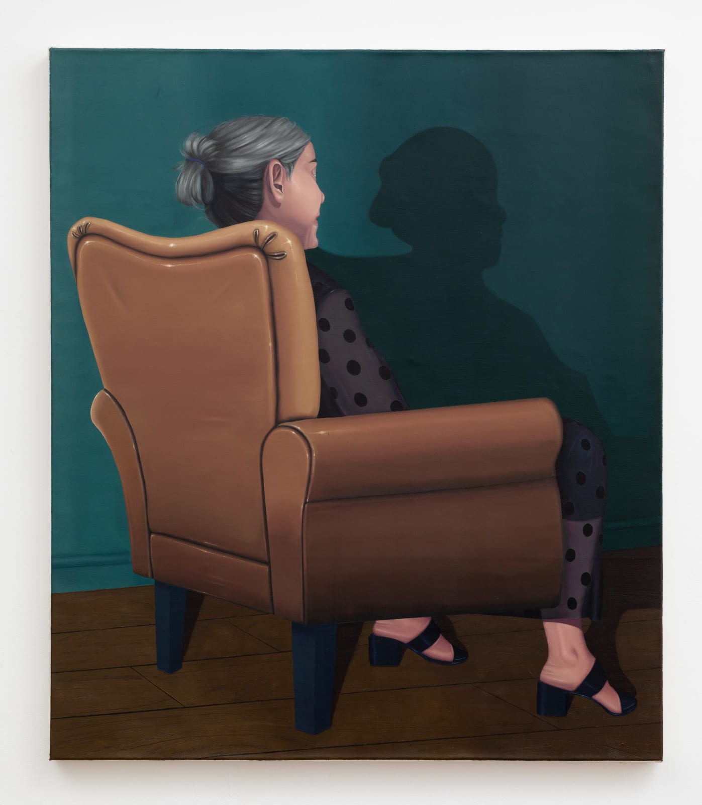 Painting portraying an older woman sitting on a brown leather chair, her back turned to the viewer, seemingly effortlessly holding up the chair with her feet, and staring at her shadow on a mallard green wall.