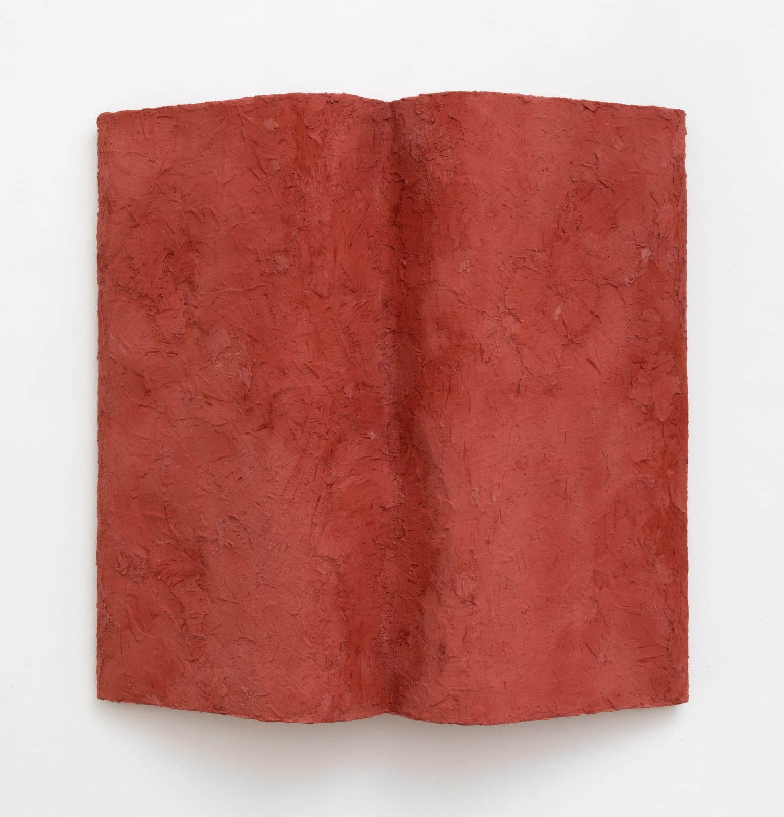 Wall-mounted sculpture in the shape of an open book that is uniformly covered with red stucco relief texture.