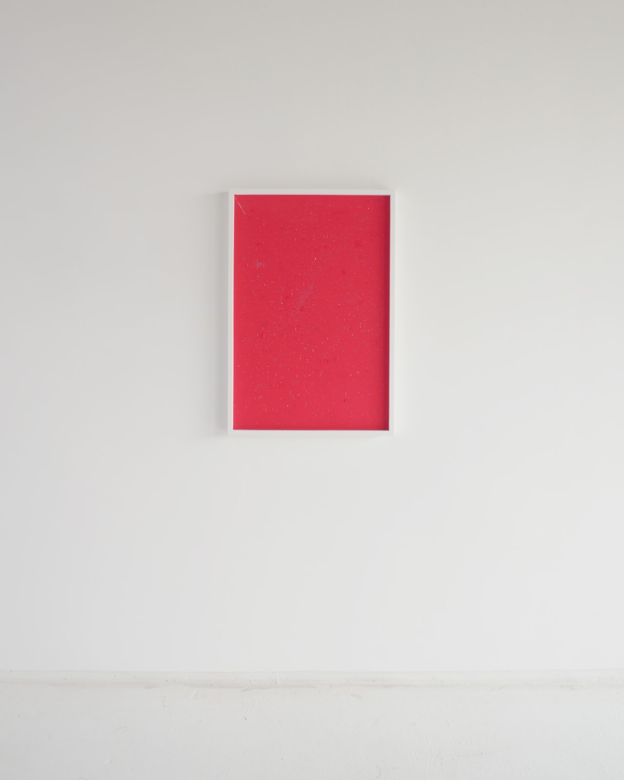 A red vertical rectangle with white, black, and red 1D and 3D cutouts and flaps in a white frame hanging on a white wall.