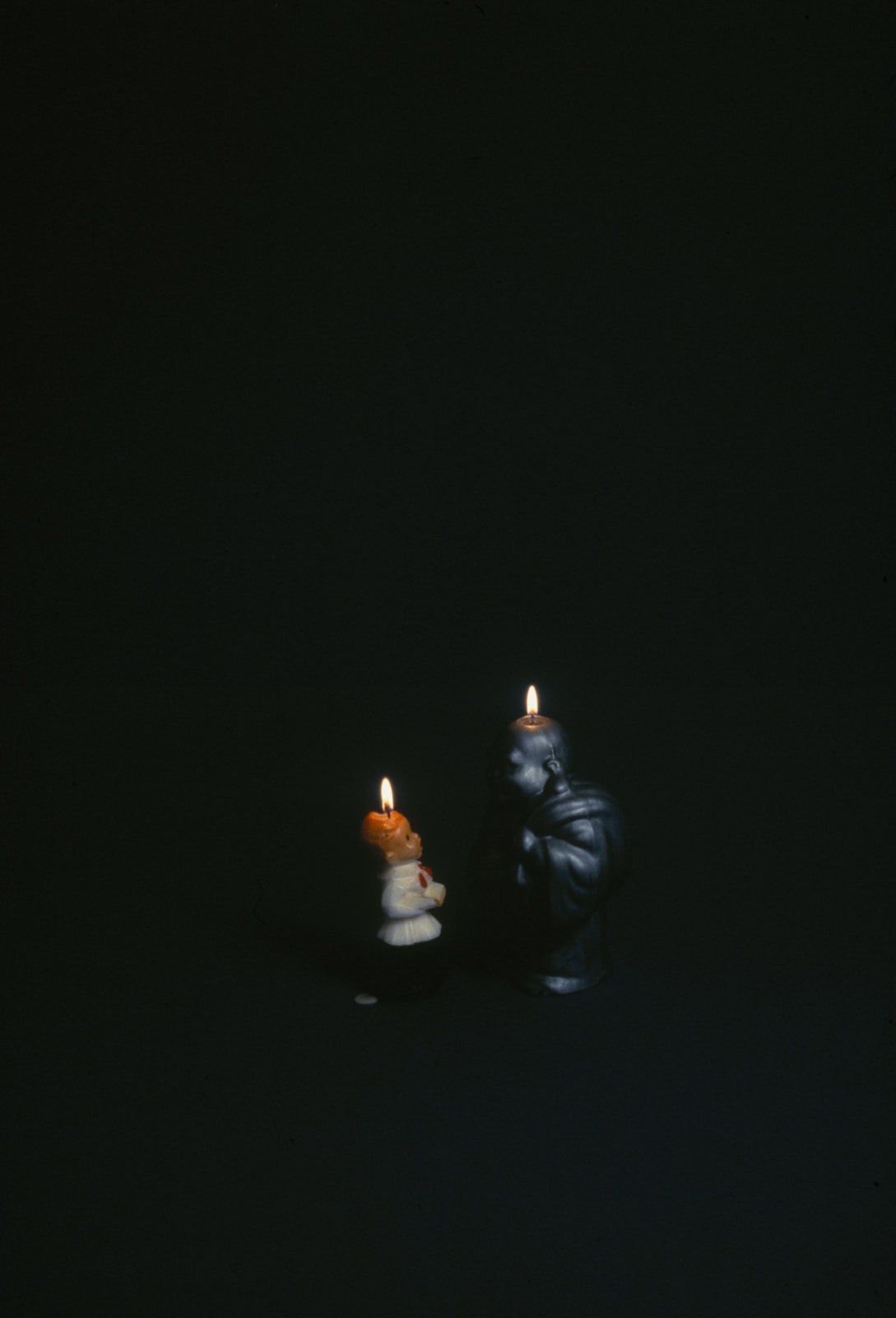 Cibachrome print of a digital photograph which depicts two different lit figurine candles. The two candles face each other and stand in front of a black background
