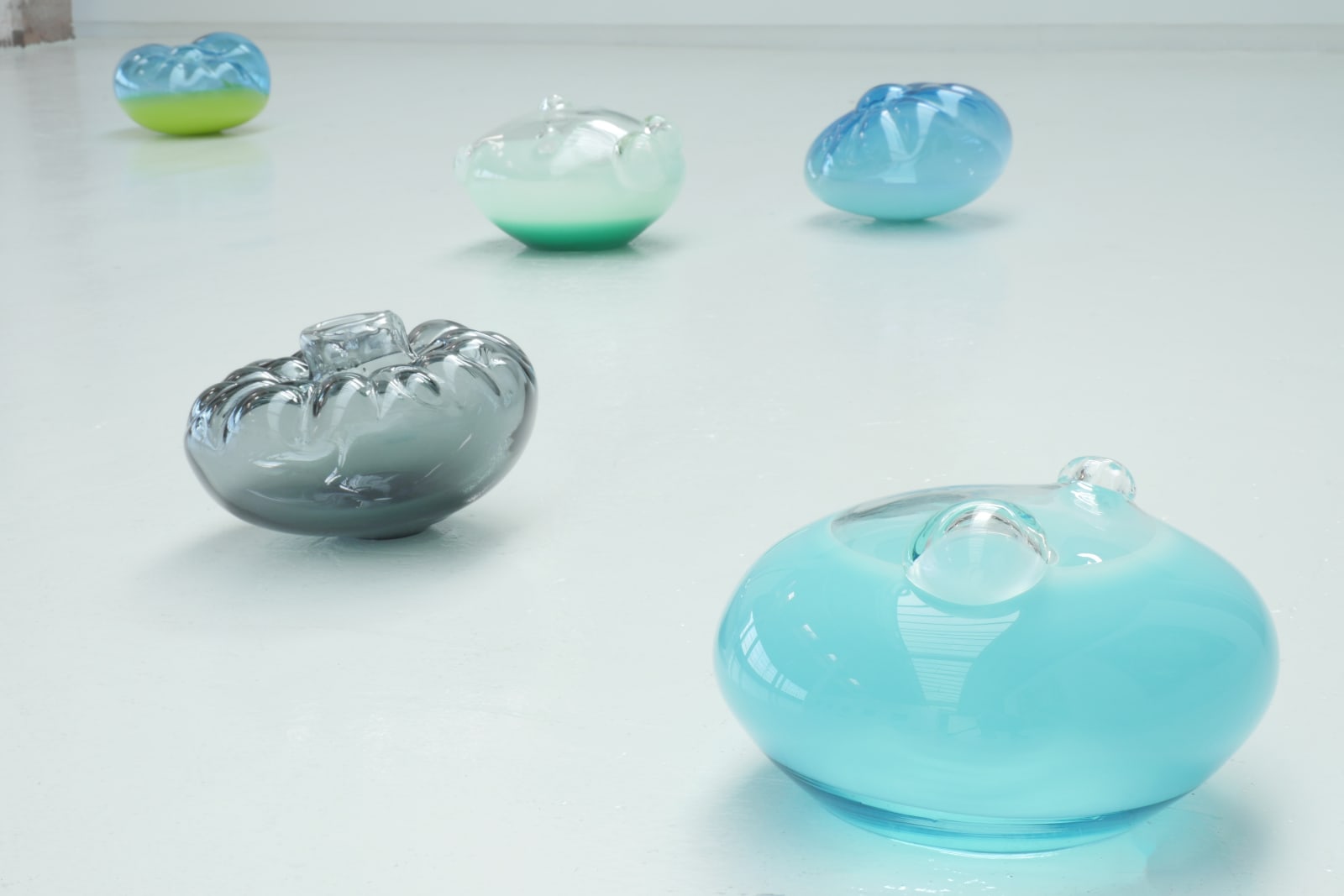 Five glass blown sculptures arranged on a white floor.