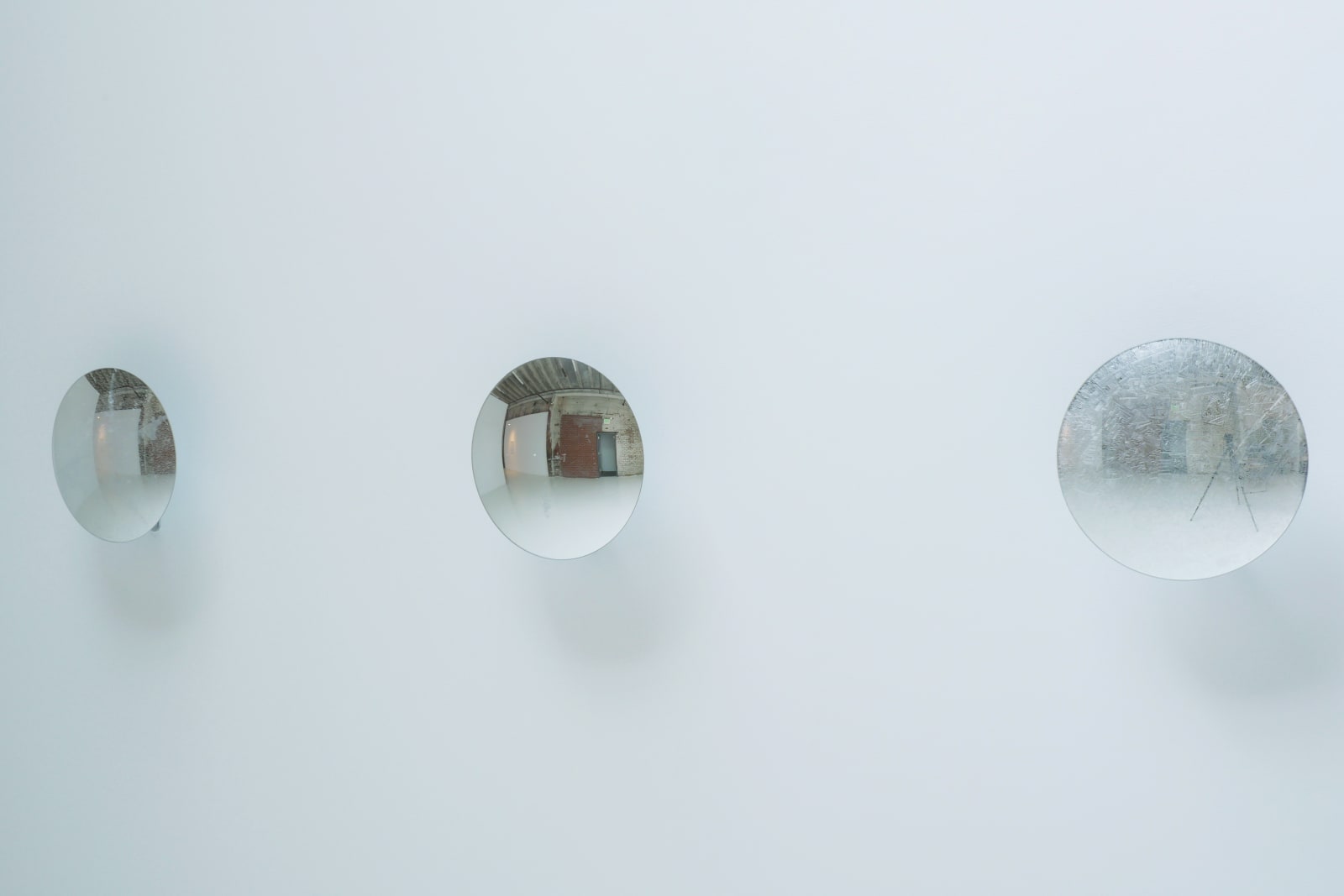 Side angled view of three reflective disks mounted in a row on a white wall.