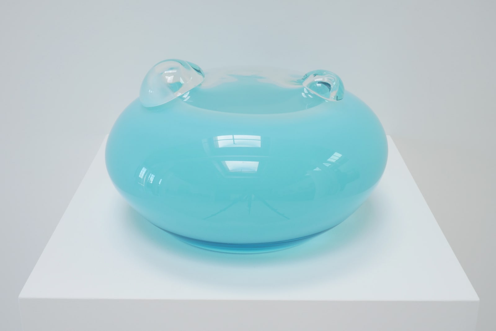 A light blue UFO-shaped sculpture with two clear bubbles on top, on a white pedestal.