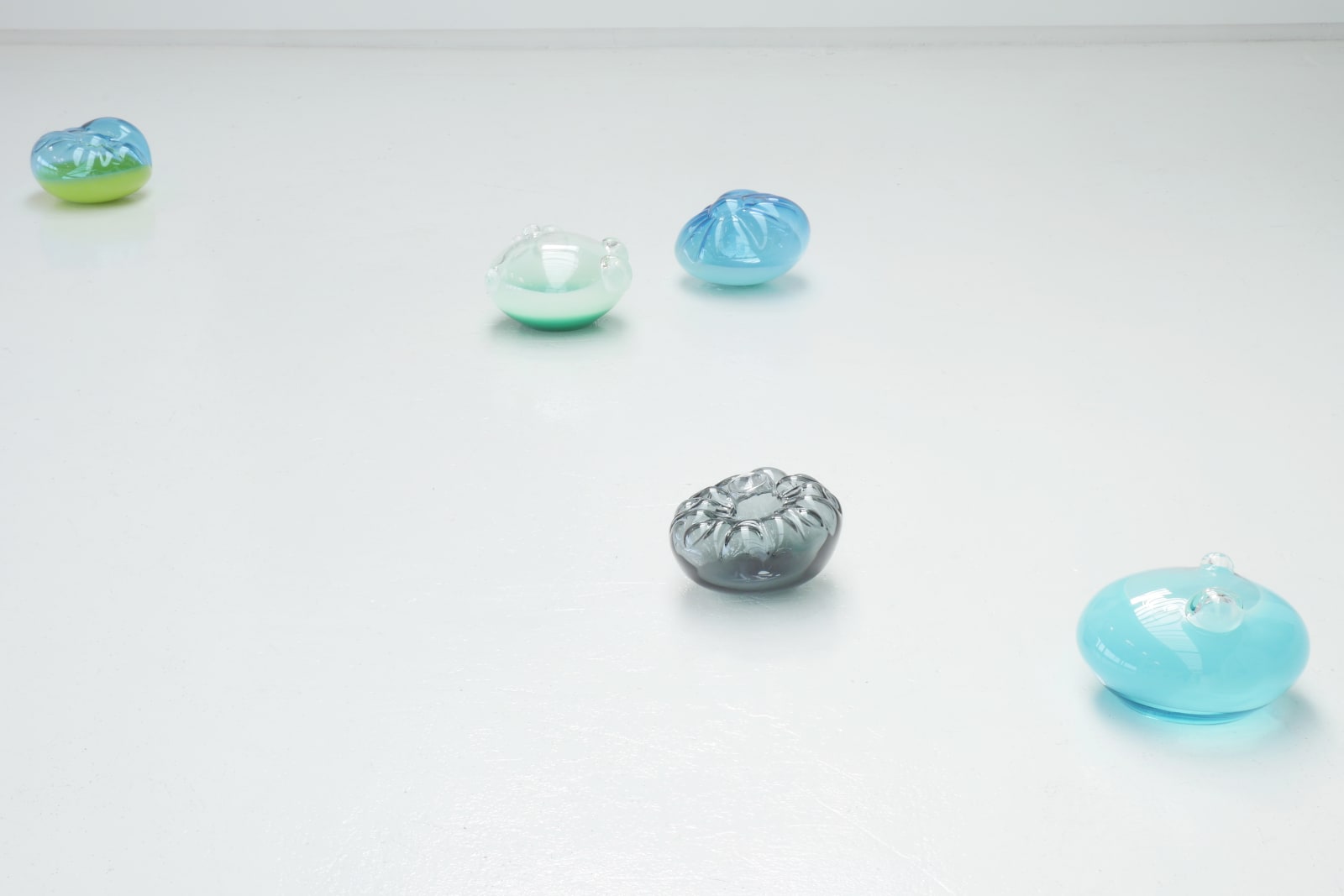 Five glass blown sculptures arranged on a white floor.