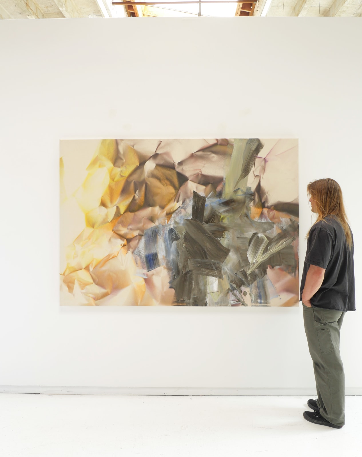 White man observes painting hanging on white wal.