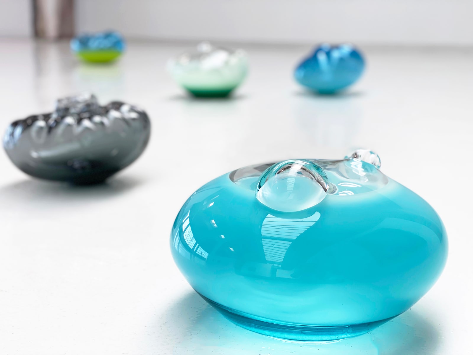 Five glass blown sculptures arranged on a white floor.